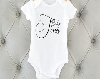 May include: White baby onesie with black text that reads "Baby Jones" in a cursive font.