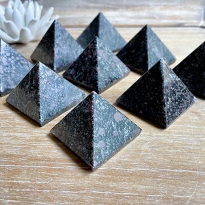 May include: Eight dark gray and pink speckled pyramid-shaped crystals on a wooden surface.