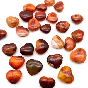 May include: A collection of carnelian heart-shaped stones. The stones are various shades of orange and red with white banding.