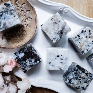 May include: Six polished, white and black, cube-shaped labradorite crystals on a white tray. The crystals are arranged in a semi-circle.