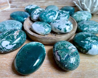 May include: A collection of green and white moss agate tumbled stones. The stones are smooth and polished, with a variety of patterns and textures.