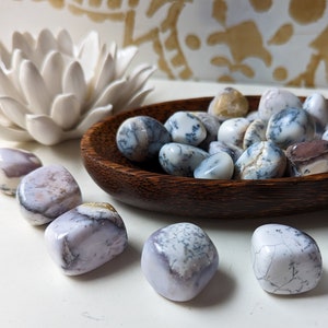 May include: A collection of white and gray dendritic agate tumbled stones in a wooden bowl. The stones are smooth and polished, with a variety of patterns and shapes.