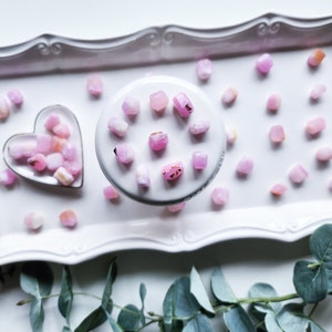 May include: A white heart-shaped dish filled with small pink and white crystals, surrounded by more crystals on a white tray with a decorative edge.