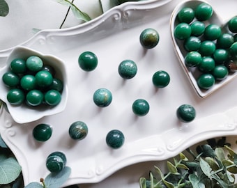 May include: A white tray with a heart-shaped dish filled with green malachite spheres.  The tray also has several green malachite spheres scattered on it.  There is a small white bowl with more green malachite spheres.