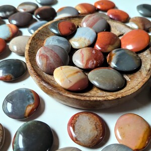 May include: A collection of polished, colorful, and patterned agate stones. The stones are various shades of red, brown, gray, and white. Some of the stones are arranged in a wooden bowl.