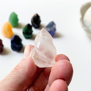May include: A clear quartz crystal shaped like a swirl, with a smooth, polished surface. The crystal is being held in a hand.