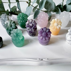 May include: A collection of ten small, carved flower pots made of various stones. The pots are in different colors, including green, purple, pink, white, and yellow. Each pot has a small flower carved on top.