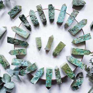 May include: A collection of green and brown crystal points arranged in a circle on a white surface. The points are all roughly the same size and shape, and they have a natural, rough texture.