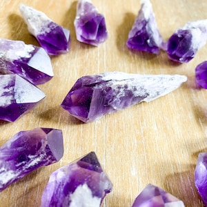 May include: A collection of amethyst crystal points, with a purple and white color scheme, arranged in a circle on a wooden surface.