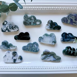 May include: A collection of 12 green, white, and black agate cloud-shaped stones on a white background.