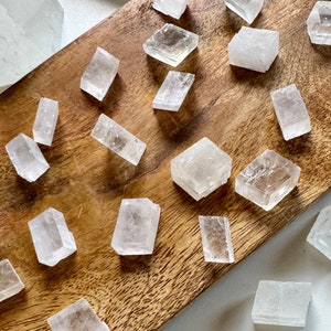 May include: A collection of clear, natural selenite crystals of various shapes and sizes, arranged on a wooden surface.