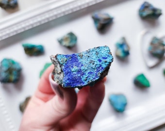 May include: A close-up of a blue and green mineral rock. The rock has a rough, irregular shape and is held in a hand.