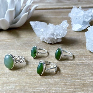 May include: Three silver rings with green oval stones. The rings are on a wooden surface with white crystal clusters.