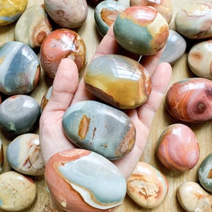 May include: A collection of polished, multi-colored, oval-shaped stones. The stones have a variety of patterns and colors, including red, orange, yellow, green, blue, and brown.