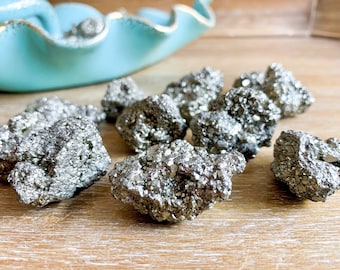 May include: A group of small, rough, silver-colored pyrite crystals on a wooden surface. The crystals have a metallic sheen and are irregularly shaped.