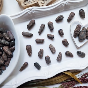 May include: A white ceramic tray with a heart-shaped dish filled with small, dark red, rough-cut gemstones. The tray is also filled with similar gemstones, some of which are arranged in a line.