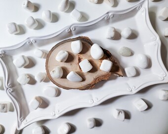 May include: A collection of white tumbled stones on a white plate and a wooden slice. The stones are smooth and polished, and they are arranged in a pleasing pattern.
