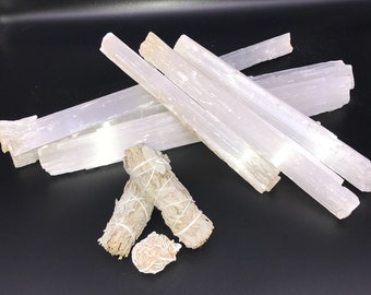 May include: A group of white selenite sticks and two white sage smudge sticks on a black background.