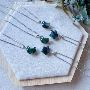 May include: Five silver necklaces with green agate pendants in the shapes of crescent moons and stars. The necklaces are displayed on a wooden surface.