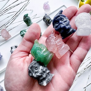 May include: A collection of small, hand-carved gnome figurines made from various types of semi-precious stones. The gnomes are in various colors, including green, pink, gray, and blue.