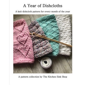 May include: Four knitted dishcloths in pink, multicoloured, teal and white. The dishcloths are laid out on a wooden surface with knitting needles and a measuring tape. The text "A Year of Dishcloths" and "A pattern collection by The Kitchen Sink Shop" is visible.