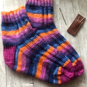 Peut inclure: Une paire de chaussettes tricotées à la main avec un motif rayé de violet, bleu, orange et rose.