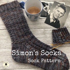Peut inclure: Une paire de chaussettes tricotées grises et orange avec un motif de point de câble. Les chaussettes sont disposées sur une surface en bois avec une tasse de café et une photographie vintage. Le texte "Simon's Socks Sock Pattern" est imprimé sur l'image.