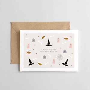 May include: A white card with a light gray background and a Halloween-themed design. The card features a witch's hat, ghosts, bones, and leaves. The text on the card reads "I got 99 problems, but a witch ain't one."