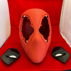 May include: A bright orange textured full-head mask featuring large eye openings with visible circular mounting points for lenses. Two separate black eye-piece inserts with white mesh detailing are positioned on either side of the mask.