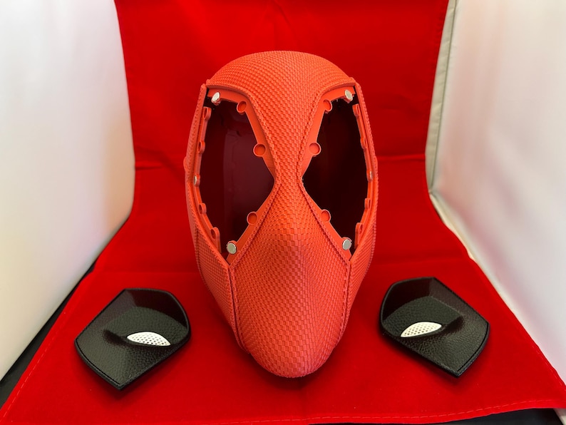 May include: A bright orange textured full-head mask featuring large eye openings with visible circular mounting points for lenses. Two separate black eye-piece inserts with white mesh detailing are positioned on either side of the mask.