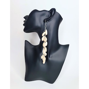 May include: Long white shell earrings with a silver chain. The earrings are hanging from a black mannequin head.