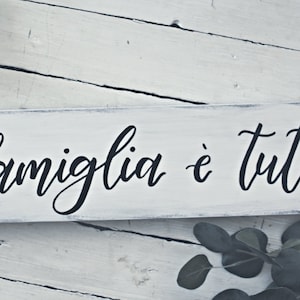 May include: White wooden sign with black calligraphy that reads "La famiglia è tutto".