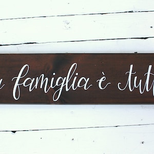 May include: A dark brown wooden sign with white lettering that reads "La famiglia è tutto".