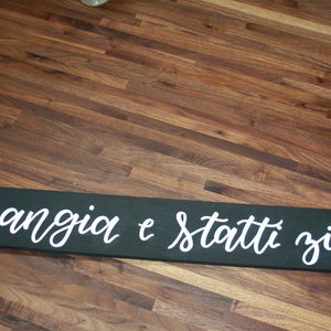 May include: A black wooden sign with white lettering that reads "mangia e statti zitto".