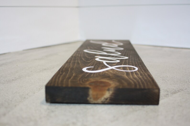 Puede incluir: Un letrero rectangular de madera te&ntilde;ida oscura con la palabra "Laundry" en letras cursivas blancas. La veta de la madera es visible y el letrero se ve desde un &aacute;ngulo bajo.