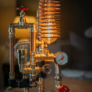 May include: A steampunk-style table lamp made from copper and brass pipes. The lamp features a coiled copper wire light fixture with a clear glass bulb and a brass gauge.