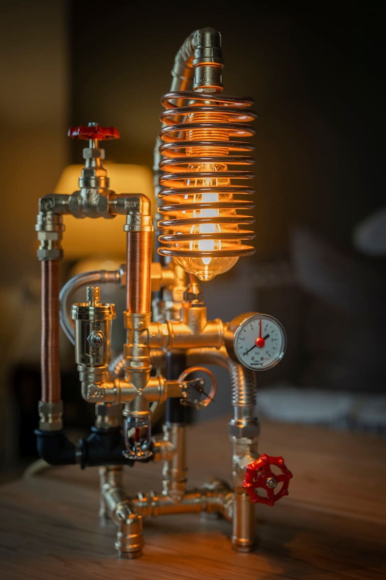 May include: A steampunk-style table lamp made from copper and brass pipes. The lamp features a coiled copper wire light fixture with a clear glass bulb and a brass gauge.