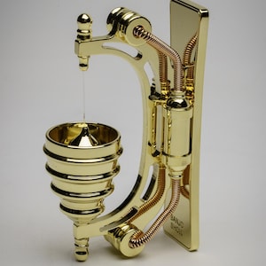 May include: A gold-toned metal wall-mounted doorbell with a bell shaped like a cone. The doorbell has a decorative design with intricate details and a copper-colored wire.