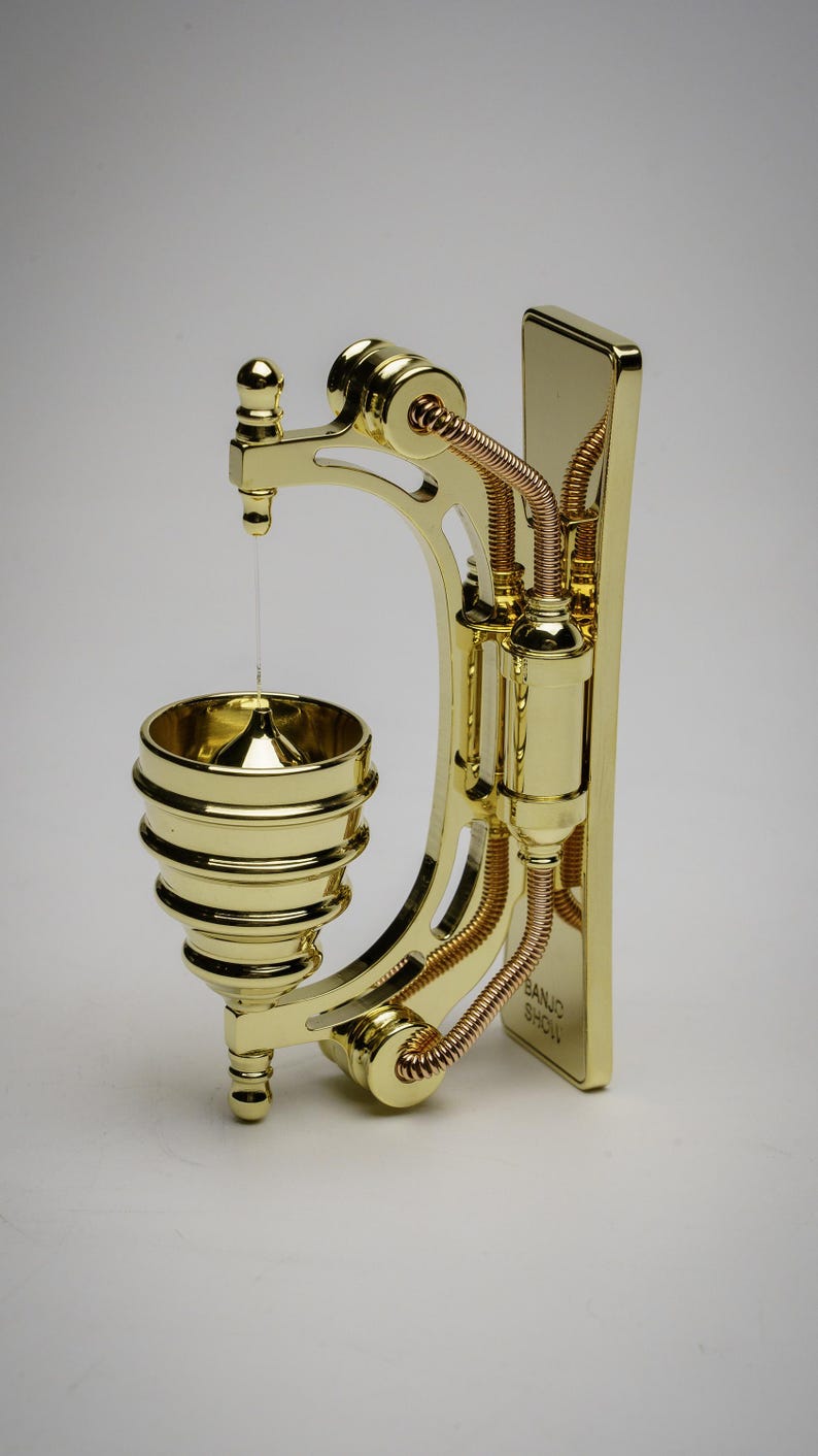 May include: A gold-toned metal wall-mounted doorbell with a bell shaped like a cone. The doorbell has a decorative design with intricate details and a copper-colored wire.