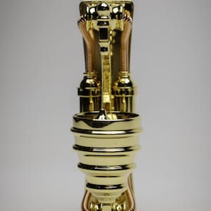 May include: A gold-colored metal decorative stand with a round top and three legs. The stand has a steampunk design with pipes and gears.