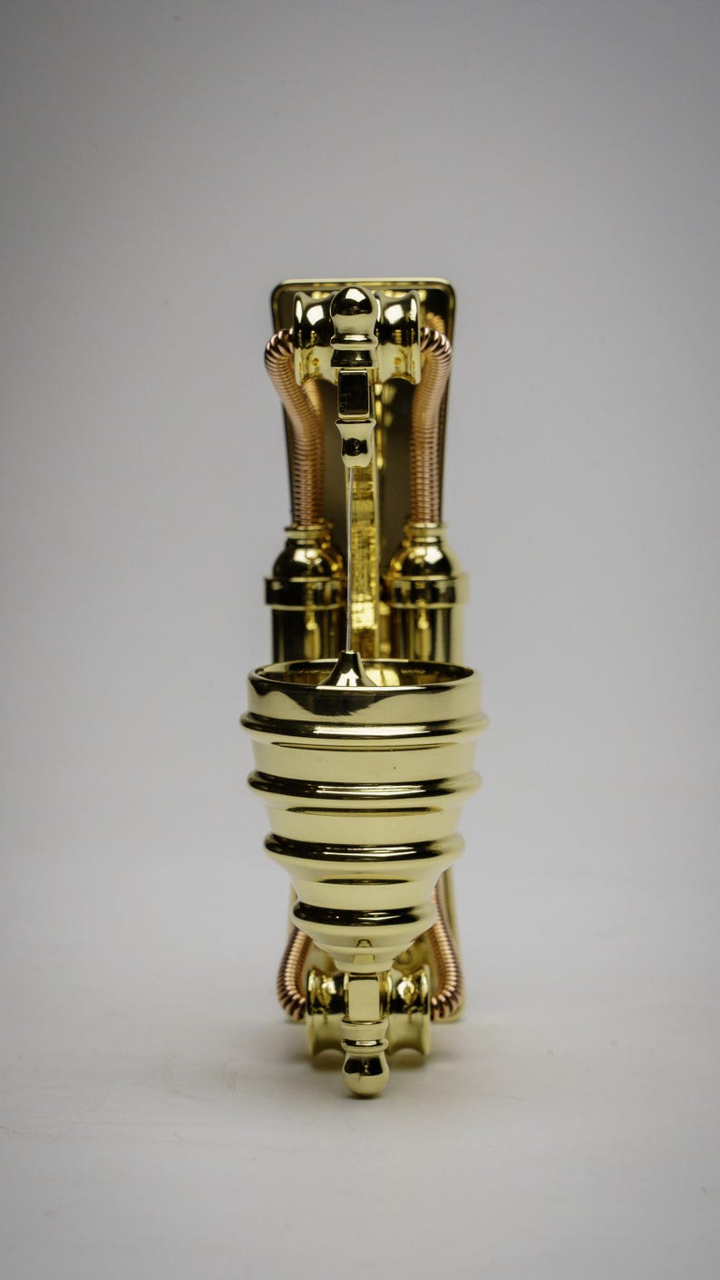 May include: A gold-colored metal decorative stand with a round top and three legs. The stand has a steampunk design with pipes and gears.