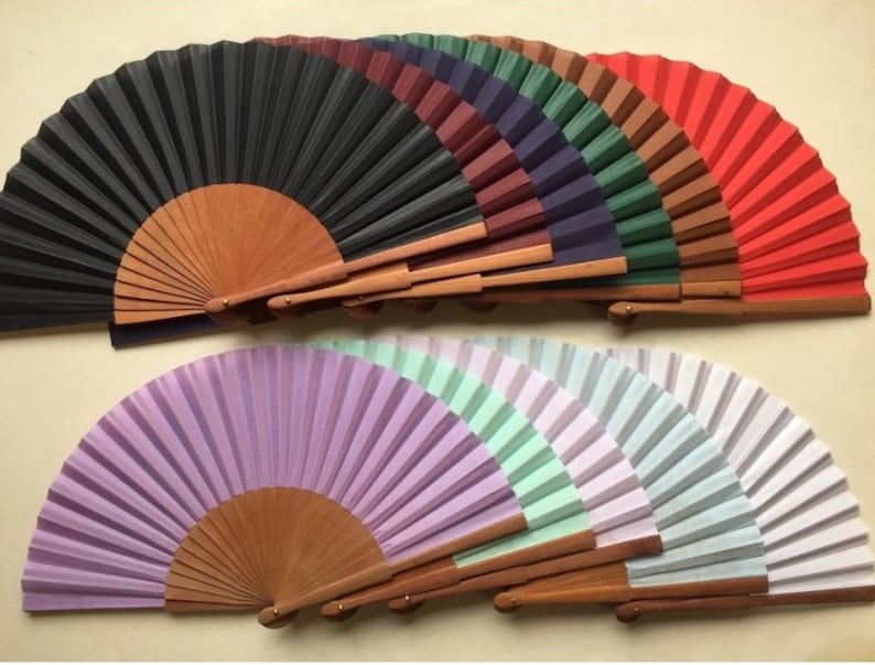 May include: A set of ten hand fans with wooden handles. The fans are made of paper and come in a variety of colors, including black, red, purple, green, and white.