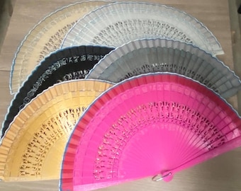 May include: A set of six decorative folding fans in various colors, including black, gold, gray, pink, and white. The fans are made of wood and have intricate designs.