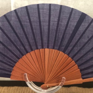 May include: A blue fabric hand fan with a wooden frame. The fan is closed and has a dark blue fabric with black stripes.