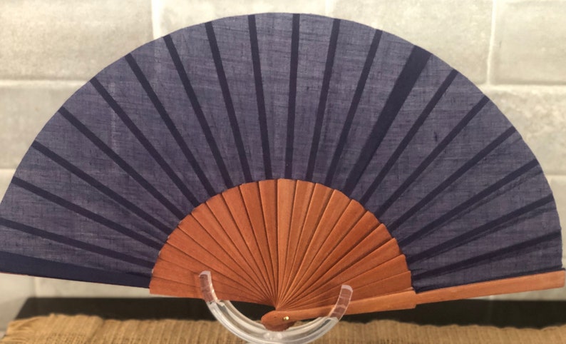 May include: A blue fabric hand fan with a wooden frame. The fan is closed and has a dark blue fabric with black stripes.