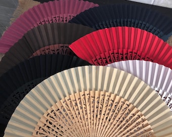 May include: A collection of hand fans in various colors, including red, black, brown, and beige. The fans are made of fabric and have a wooden frame. Some of the fans have intricate designs carved into the wood.