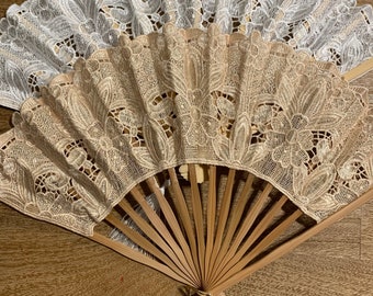 Puede incluir: Un conjunto de dos abanicos plegables decorativos con marco de madera y tela de encaje. Los abanicos son de color blanco y beige con un patrón floral. El abanico tiene un borla dorada.