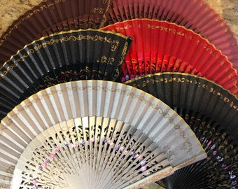 May include: A set of four hand fans with intricate gold designs. The fans are made of paper and have a variety of colors, including black, red, and white.
