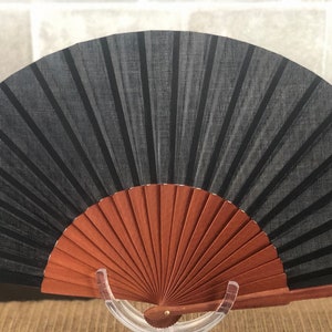 May include: A black fabric hand fan with a wooden frame. The fan is closed and has a brown wooden handle.