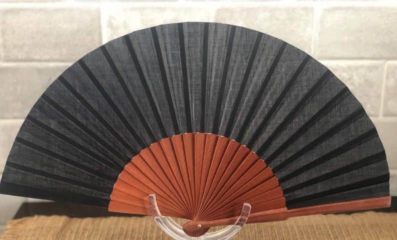 May include: A black fabric hand fan with a wooden frame. The fan is closed and has a brown wooden handle.
